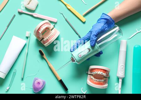 Weibliche Hand in medizinischen Handschuhen mit Mundspüler und verschiedenen Zahnhygienewerkzeugen auf türkisfarbenem Hintergrund Stockfoto