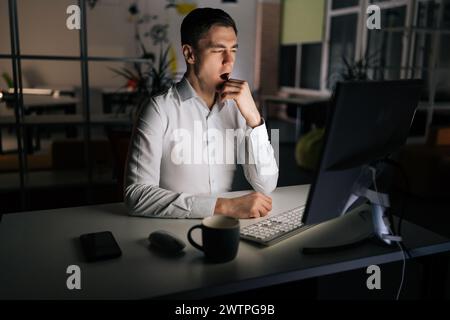 Porträt eines müden männlichen Beamten, der während der Benutzung des Computers gähnt und sich nach einem Überarbeitungsprojekt über Nacht schläfrig fühlt. Erschöpfter Geschäftsmann Stockfoto