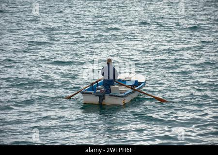 Fischer mit einem Ruderboot und in blauen Overalls Reihen mit dem Rücken zur Kamera Stockfoto