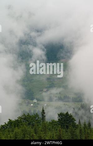 Dichter Nebel in den Bergen, durch den die Häuser und das Dorf kaum sichtbar sind. Stockfoto