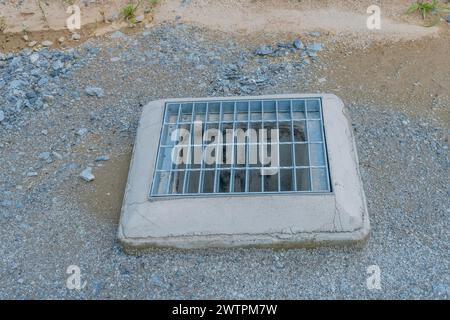 Ein quadratisches Abflussgitter aus Beton, umgeben von Kieselsteinen am Straßenrand, in Daejeon, Südkorea, Asien Stockfoto