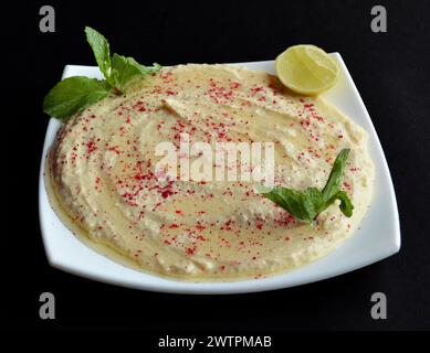 Hummus ist ein glattes und cremiges Püree aus gekochten Kichererbsen (Garbanzo-Bohnen), Tahini und typischerweise Zitronensaft. Eine Nahaufnahme auf schwarzem Hintergrund Stockfoto