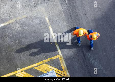 Zwei Bauarbeiter in Schutzhüten gehen über den Asphalt. Sie werfen lange Schatten. Stuttgart, Baden-Württemberg, Deutschland Stockfoto