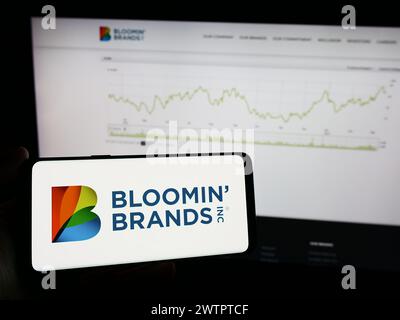 Person mit Mobiltelefon mit Logo der amerikanischen Restaurant-Holding Bloomin' Brands Inc. Vor der Webseite. Schwerpunkt auf dem Display des Telefons. Stockfoto