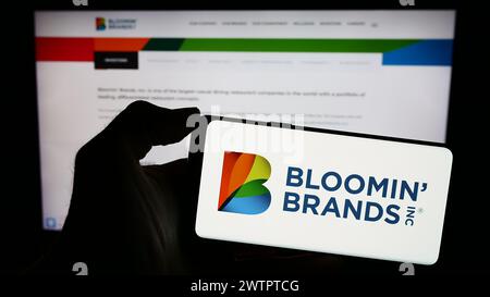 Person mit Smartphone und Logo der US-Restaurantholding Bloomin' Brands Inc. Vor der Website. Schwerpunkt auf dem Display des Telefons. Stockfoto