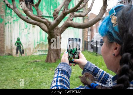 Am 18. März 2024 bewundert die Öffentlichkeit ein neues Kunstwerk des mysteriösen Künstlers Banksy an der Hornsey Road im Norden Londons. Das neue Stück erschien am Wochenende, aber heute beanspruchte der Künstler die Anerkennung für dieses neueste Werk - ein grünes Spray auf einer Wohnwand hinter einem getrimmten Baum, der wie Laub aussieht, mit einer Schablone einer Person, die einen Druckschlauch daneben hält. Stockfoto