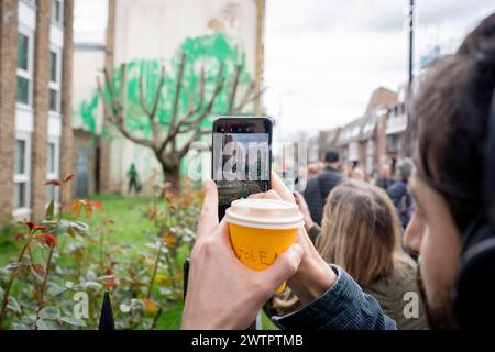 Am 18. März 2024 bewundert die Öffentlichkeit ein neues Kunstwerk des mysteriösen Künstlers Banksy an der Hornsey Road im Norden Londons. Das neue Stück erschien am Wochenende, aber heute beanspruchte der Künstler die Anerkennung für dieses neueste Werk - ein grünes Spray auf einer Wohnwand hinter einem getrimmten Baum, der wie Laub aussieht, mit einer Schablone einer Person, die einen Druckschlauch daneben hält. Stockfoto