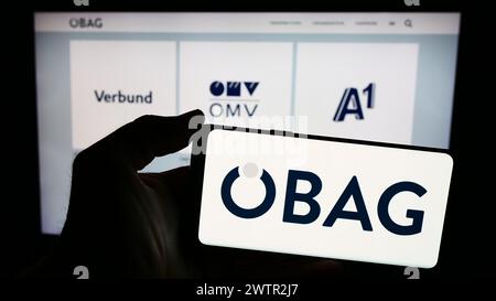 Person mit Smartphone mit Logo der Österreichischen Beteiligungs AG (ÖBAG) vor der Website. Schwerpunkt auf dem Display des Telefons. Stockfoto
