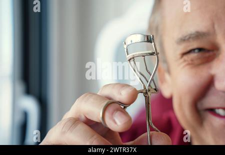 Mann, der Mascara auf die Wimpern legt. Reifer Transgender-Mann mit Make-up, der vor der Kamera lächelt Stockfoto