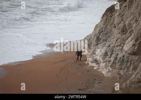 Mann und Frau gehen neben den Kalksteinklippen, Teil der Jurassic Coast in der Nähe von Durdle Door im März, Dorset, England, Großbritannien Stockfoto