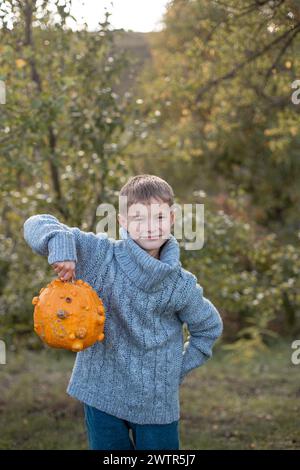 Junge in einem gestrickten blauen Pullover hält hässliche orange Kürbisse in den Händen. Deformierte orangefarbene Kürbisse mit beschädigter, hässlicher Haut. Thanksgiving, Ernte, halloween-Konzept. Stockfoto