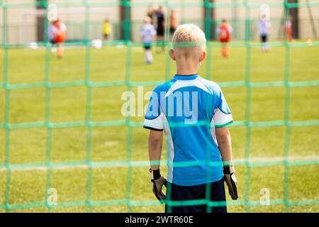 Kleiner Junge in Torwartuniform und Handschuhen, die in einem Fußballtor stehen. Kinder spielen Fußballspiel auf dem Schulsportplatz Stockfoto