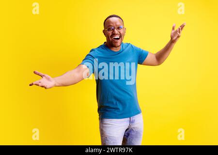 Glücklicher und aufgeregter afroamerikanischer Mann, der lächelt und Hände vor gelbem Studiohintergrund spreizt. Positive Überraschung Stockfoto