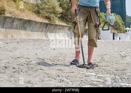 Ein Mann mit einem Metalldetektor am Sandstrand, tagsüber im Sommer. Stockfoto