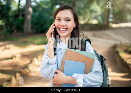 Eine fröhliche junge Frau, die ein lebhaftes Telefongespräch führte, während sie Bücher hielt Stockfoto