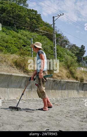 Ein Mann mit einem Metalldetektor am Sandstrand, tagsüber im Sommer. Stockfoto