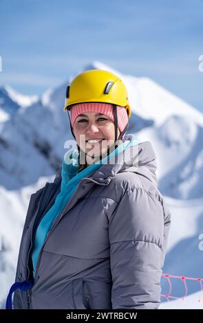 Die Retterin lächelt in einem gelben Helm und steht vor dem Hintergrund großer Berge Stockfoto