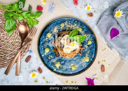 Spaghetti auf blauem Teller mit frischen Kräutern und essbaren Blumen Stockfoto