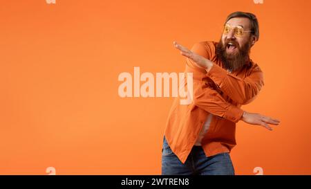 Rothaariger bärtiger Kerl in Sonnenbrille tanzt mit lustigen Bewegungen, Studio Stockfoto