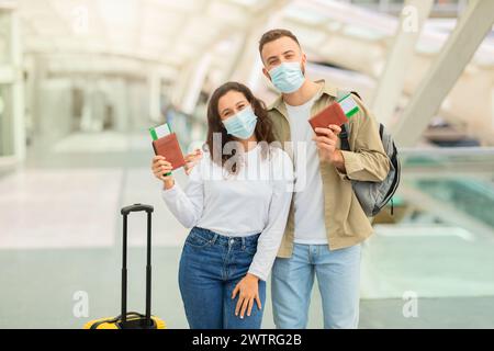 Glückliches Paar In Medizinischen Masken Posiert Am Flughafen Mit Pässen Und Tickets Stockfoto