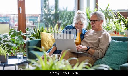 Seniorenpaar, das zu Hause auf dem Sofa sitzt und einen Laptop benutzt Stockfoto
