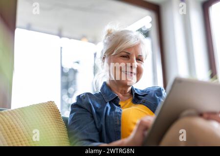 Reife Frau, die zu Hause auf dem Sofa sitzt und ein digitales Tablet verwendet Stockfoto