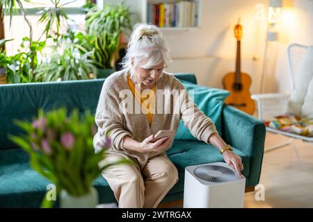 Seniorin, die ein Smartphone benutzt, um einen Luftreiniger einzurichten Stockfoto