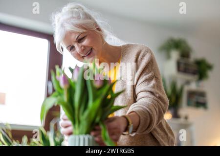 Glückliche Seniorin mit Tulpenstrauß in Vase zu Hause Stockfoto