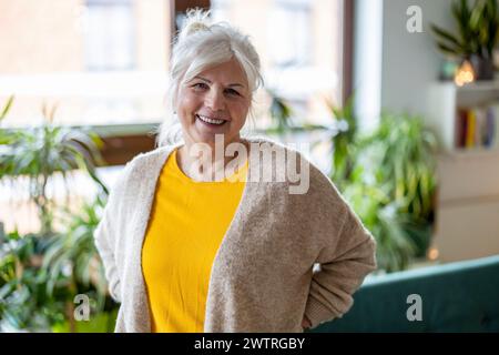 Reife Frau, die in die Kamera schaut und in ihrem Wohnzimmer zu Hause lächelt Stockfoto