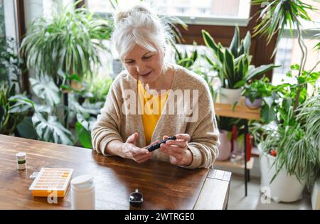 Ältere Frau, die ihren Blutzuckerspiegel überprüft, während sie zu Hause sitzt Stockfoto