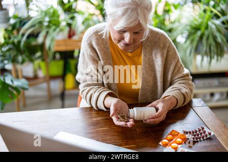 Seniorin nimmt Pillen aus einer Flasche, während sie zu Hause am Tisch sitzt Stockfoto