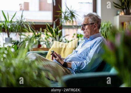 Seniorenmann, der das Handy benutzt, während er zu Hause auf dem Sofa sitzt Stockfoto
