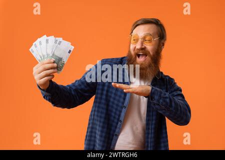 Rothaariger bärtiger Mann in Sonnenbrille, der Euro-Banknoten hält, Studio Stockfoto