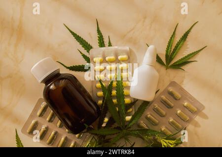 Mockups von Medikamenten auf beigem Hintergrund mit Cannabisblättern. Anordnung einer Arzneimittelflasche und einer weißen leeren Sprühflasche und Pillen auf einer Marmortabelle Stockfoto