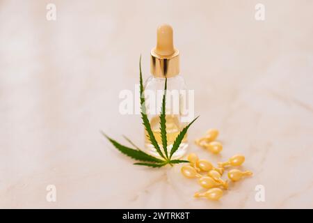 Mockup-Flasche Kosmetikprodukt mit Cannabisblättern auf beigem Hintergrund. Gelbe Kapseln mit aufhellendem, feuchtigkeitsspendendem Gesichtsserum mit Hyaluronsäure Stockfoto