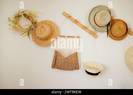 Eine weiße Wand mit Holzbügeln mit verschiedenen Strohhüten. Dekorative Dekoration im Haus. Wandbehältertasche aus Baumwollleinen und Stockfoto