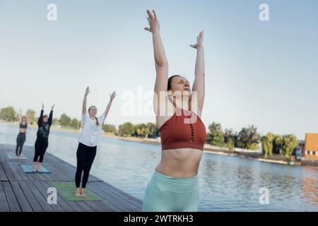 Yoga-Kurs am Morgen mit einem Lehrer am Yachthafen in der Stadt. Junge Frauen stehen mit den Händen nach oben auf den Matten und machen Übungen. Eine Gruppe von Frauen Stockfoto