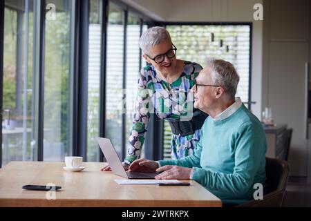 Seniorenpaar, das zu Hause einen Laptop am Tisch verwendet Stockfoto