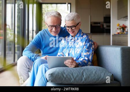 Glückliches älteres Paar, das zu Hause auf der Couch sitzt und einen Tablet-PC verwendet Stockfoto