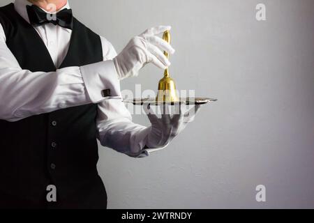 Butler oder Kellner in schwarzer Weste und weißen Handschuhen, die Bold Bell auf Serviertablett halten. Rufton für Service. Stockfoto