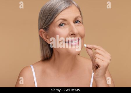 Schöne Frau, die Vitaminpille auf beigefarbenem Hintergrund nimmt Stockfoto