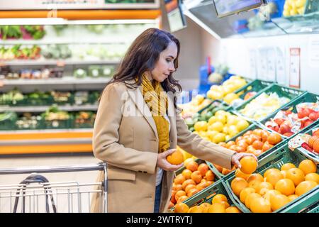 Eine Frau, die mit einem Einkaufswagen Lebensmittel kauft. Eine junge Brünette kauft Obst in einem Supermarkt. Stockfoto