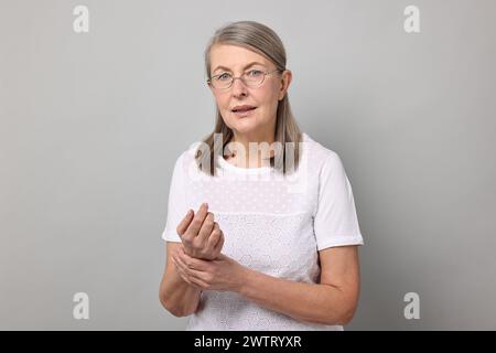 Arthritis-Symptome. Frau mit Schmerzen im Handgelenk auf grauem Hintergrund Stockfoto