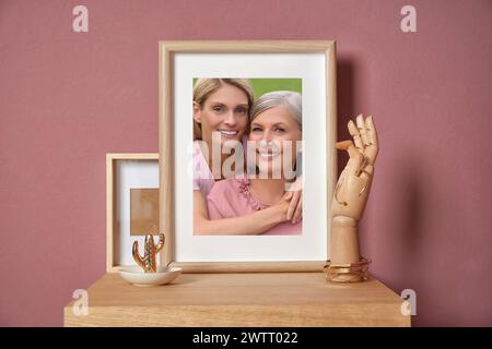 Familienporträt von Mutter und Tochter im Bilderrahmen auf Tisch in der Nähe der Farbwand Stockfoto