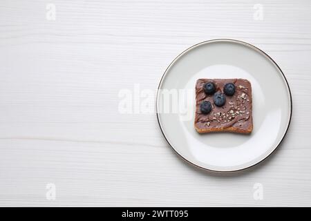 Toast mit leckerer Nussbutter, Heidelbeeren und Nüssen auf weißem Holztisch, Blick von oben. Leerzeichen für Text Stockfoto