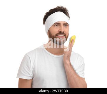 Mann mit Stirnband, der sein Gesicht mit Schwamm auf weißem Hintergrund wäscht Stockfoto