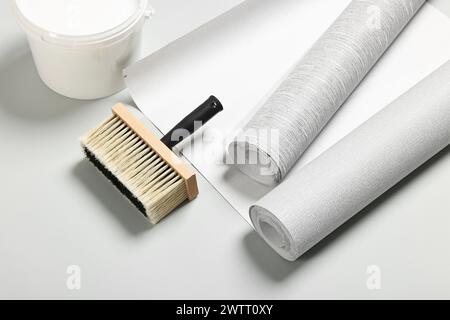 Verschiedene Tapetenrollen, Pinsel und Eimer mit Klebstoff auf hellgrauem Hintergrund Stockfoto