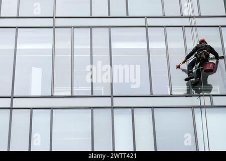 An Seilen aufgehängte Fensterreiniger reinigen die Außenfenster eines Bürogebäudes in Glasgow, Schottland. Stockfoto