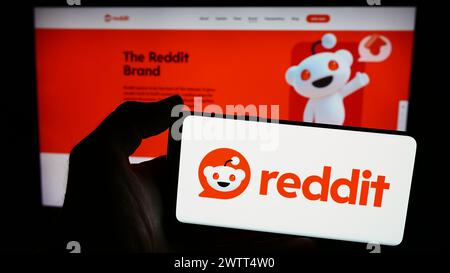 Person mit Smartphone und Logo des US-amerikanischen Social-Media-Unternehmens Reddit Inc. Vor der Website. Schwerpunkt auf dem Display des Telefons. Stockfoto