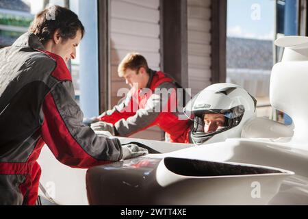 Fahrer in einem Rennwagenhelm, der sich auf das Rennen vorbereitet, während die Boxencrew im Hintergrund arbeitet. Stockfoto